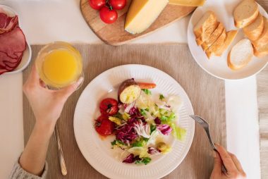 A top-view of a delicious breakfast setting featuring a salad, bread, cheese, tomatoes, and orange juice.
